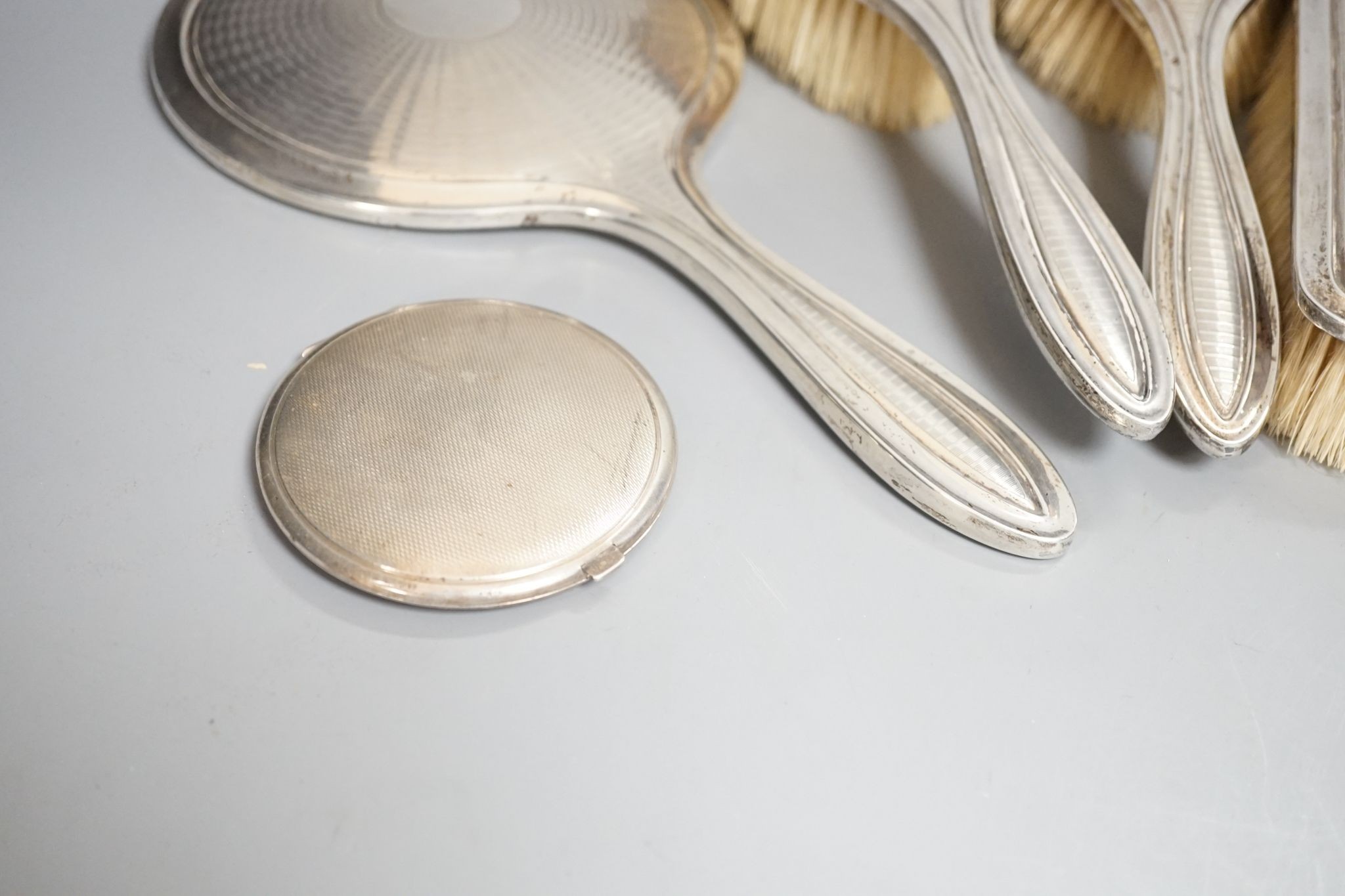 A George V engine turned silver seven piece dressing table set, comprising, two trinket boxes and a mirror, brush and comb set, Synyer & Beddoes, Birmingham, and Chester, 1912,13,14 and a silver mounted compact.